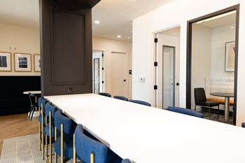 A long white table with blue chairs is in the foreground of the image.